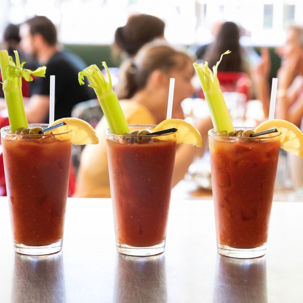 A trip of Bloody Marys on the bar with diners eating in the background.