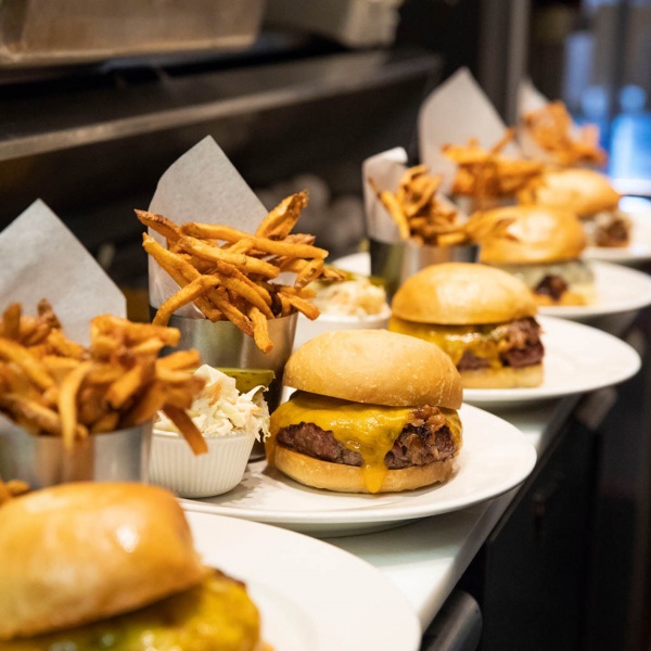 A row of 5 cheeseburgers and french fries in the kitchen on the line.