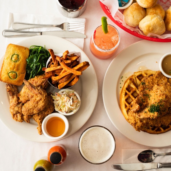 A Bird’s eye view of a dinner table: Fried Chicken Dinner with jalapeño cornbread, sautéed kale, sweet potato fries, cole slaw and honey tabasco sauce. Fried Chicken and Waffles with maple butter. A basket of buttermilk biscuits. A foamy beer. A margarita