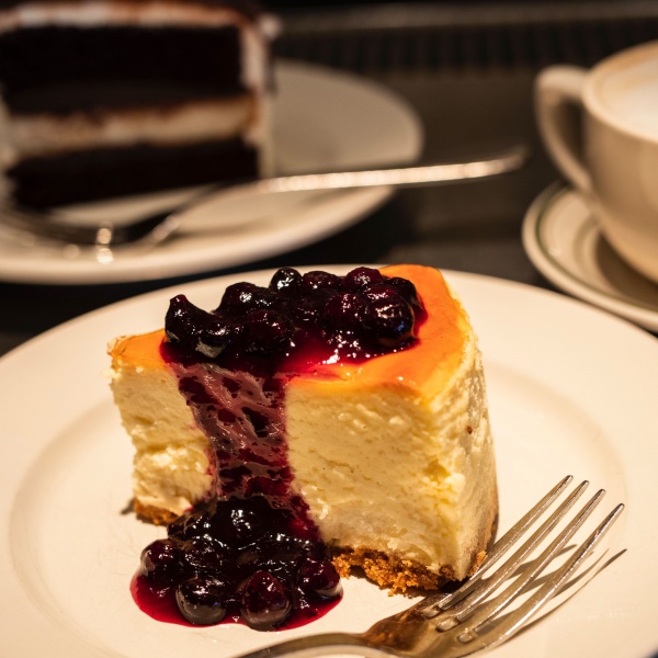 Blueberry Cheesecake on a plate with a fork. Black and White cake in the background.